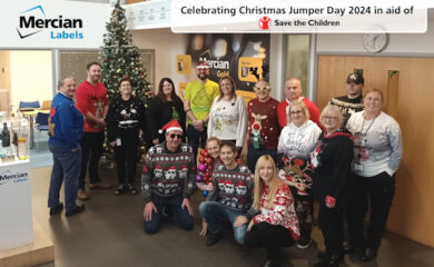 A group of people stood in front of a Christmas tree, all wearing Christmas Jumpers or festive outfits