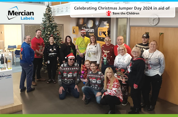 A group of people stood in front of a Christmas tree, all wearing Christmas Jumpers or festive outfits