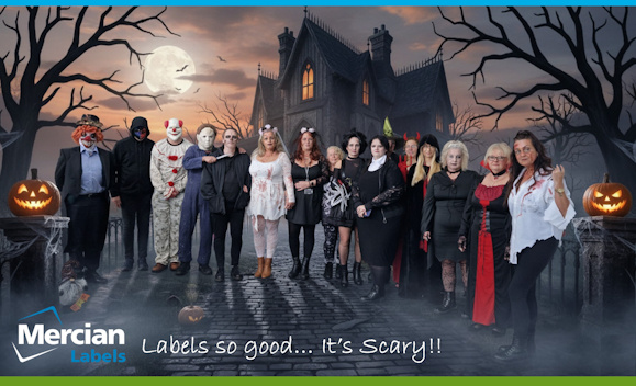 A group of Mercian Labels staff members dressed in Halloween costumes stand together in front of a spooky haunted house backdrop with a full moon, leafless trees, and glowing jack-o’-lanterns. The costumes include clowns, masked horror characters, witches, devils, gothic outfits, and zombie-like attire. The group is NOT smiling and posing for a fun company Halloween celebration. The Mercian Labels logo and the text “Labels so good… It’s Scary!!” appear at the bottom of the image.