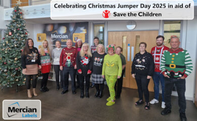 A group of Mercian Labels colleagues stood in front of a Christmas tree, all wearing Christmas Jumpers or festive outfits
